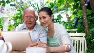 Elderly man and young woman looking at computer outdoors