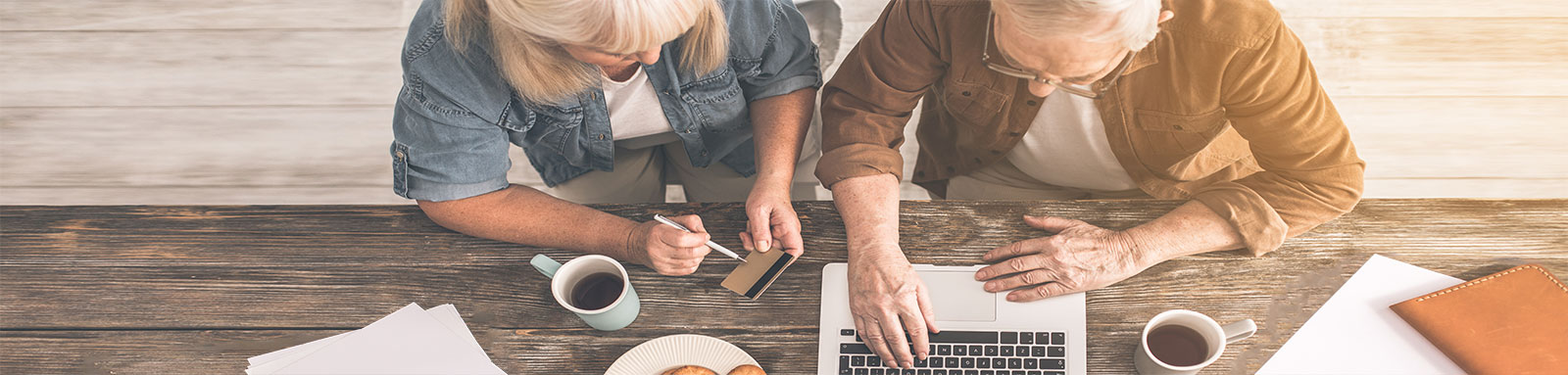 A senior couple using their credit card online with biscuits and coffee